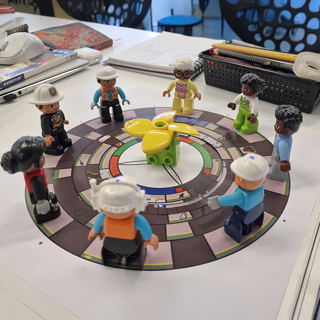 Papirversion af vores brætspils prototype med legofigurer som spillerbrikker og mølle i midten.